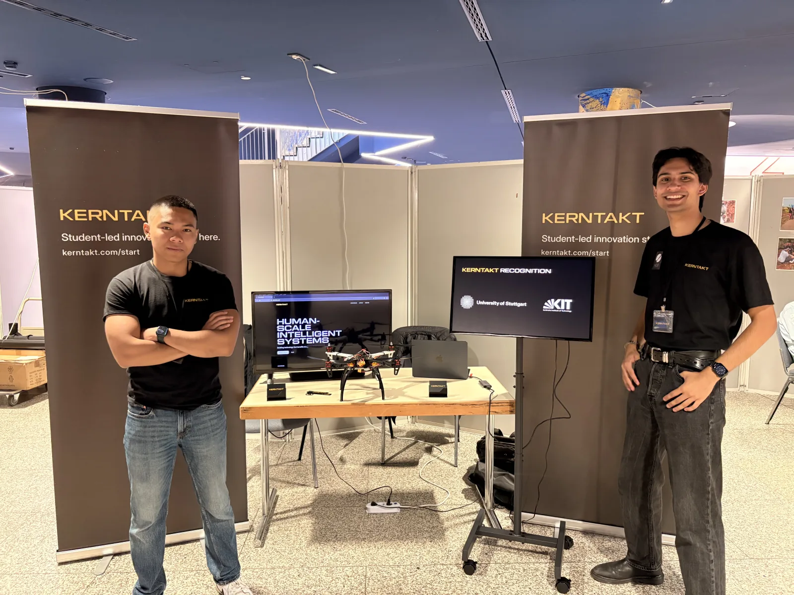 Two KERNTAKT representatives at the welcome-event booth with the ADLER drone functional prototype and display screens.